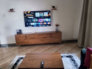Ein Wohnzimmer mit einem an der Wand befestigten Flachbildfernseher, einem Holzschrank darunter und einem Couchtisch im Vordergrund.