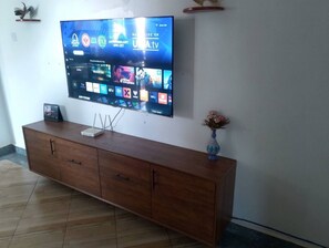 A flat-screen TV mounted on a wall above a wooden cabinet with a vase on top. - black forest courts (Kampala)