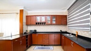 Una cocina con armarios de madera, encimera negra, salpicadero de azulejos y una ventana con persianas.
