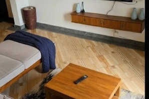 A room with a sofa, a small wooden table, a wall-mounted shelf with decorative items, and a trash can. - landville apartment Entire rental unit in Kampala, Uganda (Kampala)