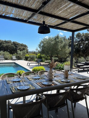 Ein Essbereich im Freien mit Pool, Korbstühle und Tisch für eine Mahlzeit.