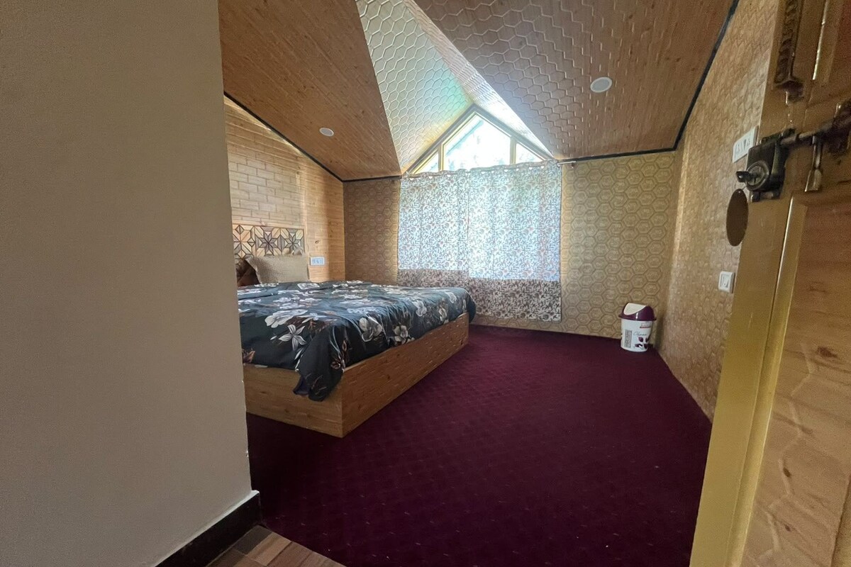 A bedroom with a sloped ceiling, a bed, a window, and a door.