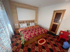 A bedroom with a wooden headboard, a patterned bedspread, a red chair, and a patterned floor. - Jahangir Cottage Pahalgam (Pahalgam)