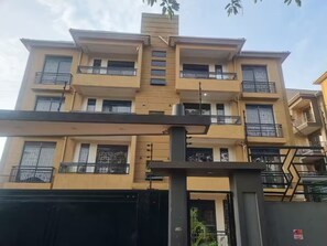 Edifício residencial com vários andares, varandas, portão e céu limpo.