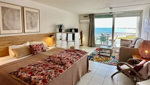 A hotel room with a bed, a desk, a chair, a balcony with a view of the sea, and framed artwork on the wall. - Studio Hotel Mont Vernon - sea view (Orient Bay)