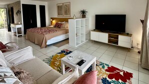 A hotel room with a bed, sofa, TV, ceiling fan, and a small table. - Studio Hotel Mont Vernon - sea view (Orient Bay)