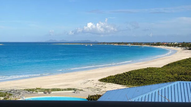 A beach view with a pool, clear sky, and distant mountains. - Studio Hotel Mont Vernon - sea view (Orient Bay)