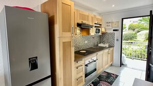 A modern kitchen with a stainless steel refrigerator, wooden cabinets, a microwave, and a tiled backsplash. - Studio Hotel Mont Vernon - sea view (Orient Bay)