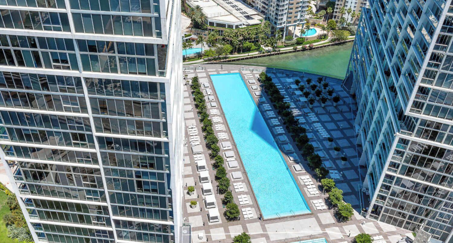 A high-rise building with a long, narrow swimming pool surrounded by lounge chairs and potted plants.