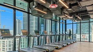 A gym with treadmills aligned against a large window overlooking a cityscape. - Modern Downtown Apartment | Group-Ready Stay (Miami)