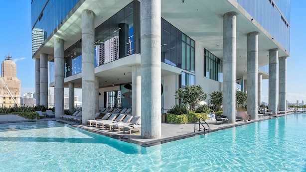 A modern building with a rooftop pool, large columns, and a view of the city skyline. - Modern Downtown Apartment | Group-Ready Stay (Miami)