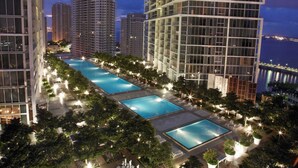 A high-rise building with a rooftop pool area, surrounded by trees and illuminated by night lights. - Spacious Group Stay | Modern Brickell Hub (Miami)