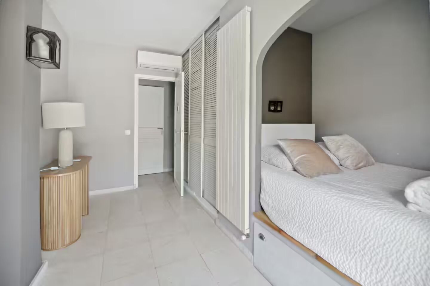 A bedroom with a bed, bedside table, lamp, and a sliding door leading to another room.