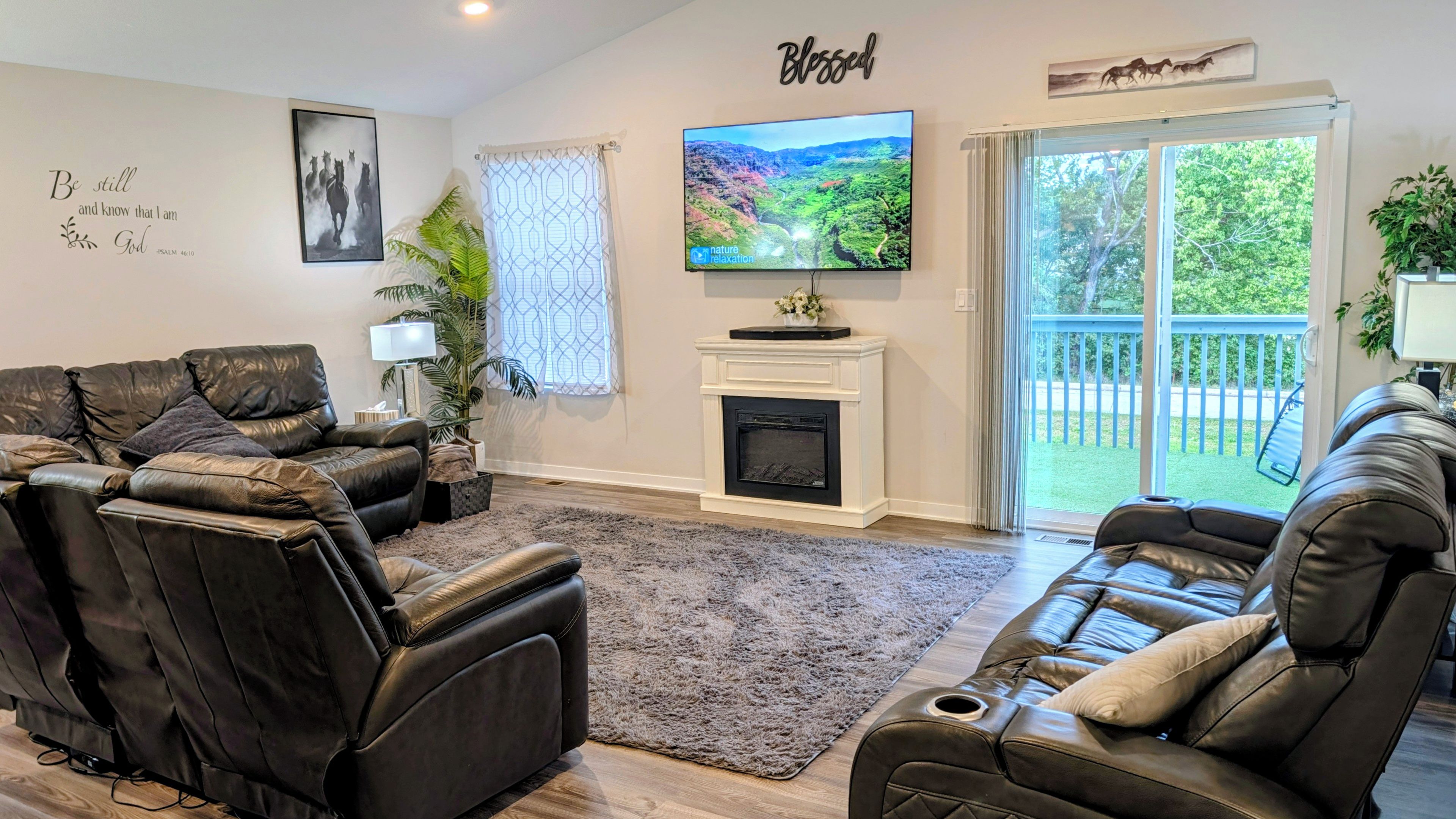 A living room with leather sofas, a fireplace, a TV, and a balcony with a view.