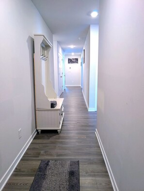 A hallway with a wooden floor, a white bench with a mirror, and a black rug.