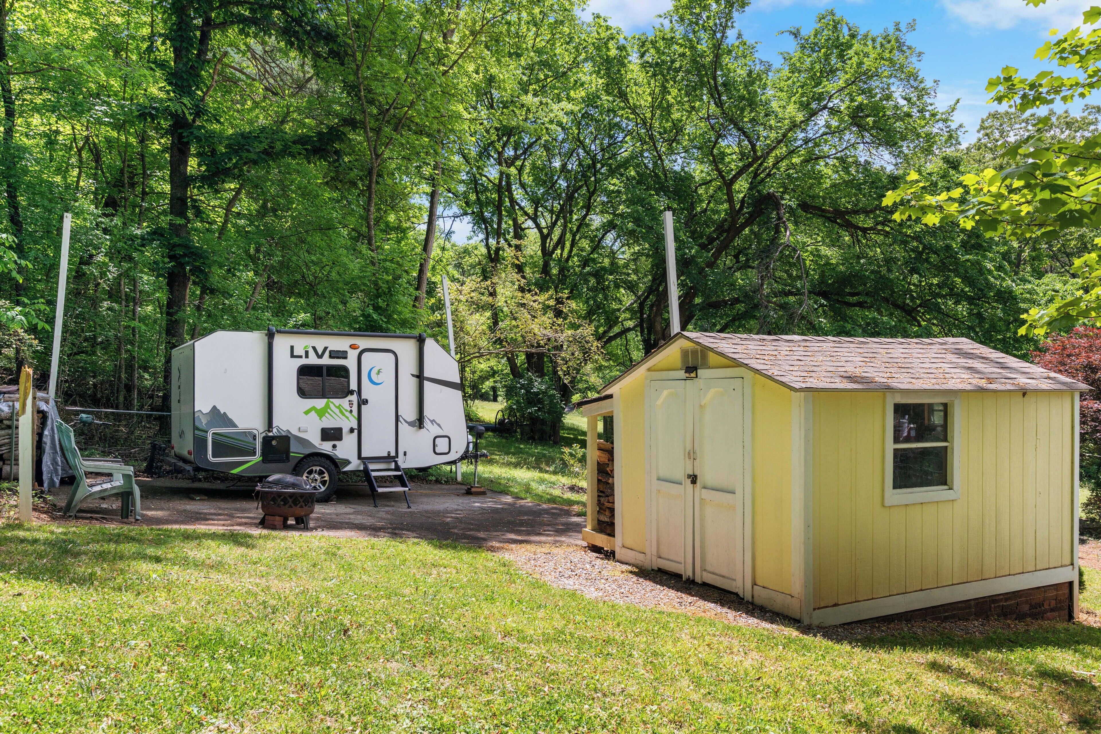 Un camping con una caravana blanca y un cobertizo amarillo pequeño.