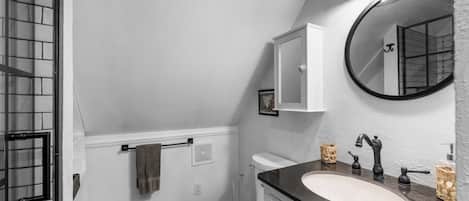 A bathroom with a white toilet, a sink with a dark countertop, a mirror, and a towel rack.