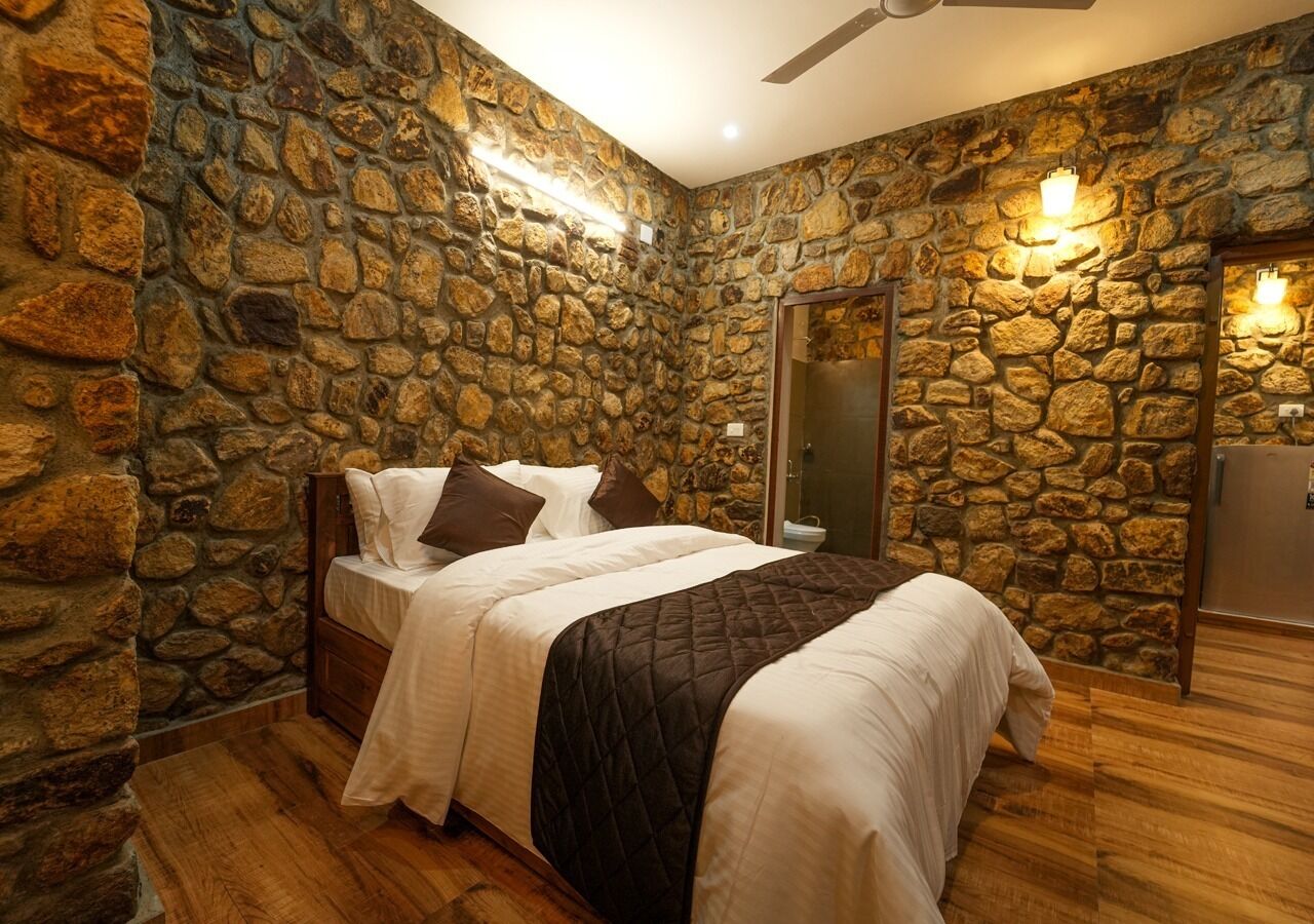 A bedroom with a stone wall, a bed with white bedding, a wooden floor, and a ceiling fan.