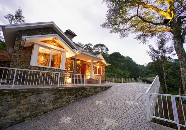 A stone house with a paved driveway and white railing. - Stone castle by voye homes (Peermade)