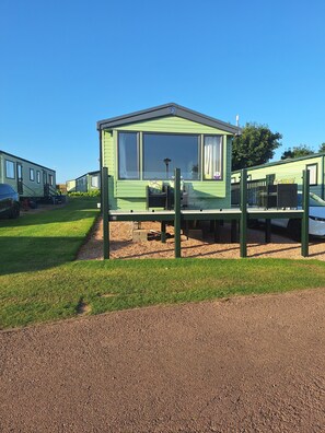 A green mobile home with a porch, a small table, and a chair. - Taigh na Mara, Holiday Home, St Andrews by the Sea (St Andrews)