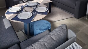 Un salon moderne avec un canapé d’angle, une table basse ronde et un coin repas aménagé pour quatre personnes.