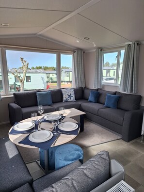 A modern living room with a sectional sofa, a round coffee table, and a dining area set for four. - Taigh na Mara, Holiday Home, St Andrews by the Sea (St Andrews)