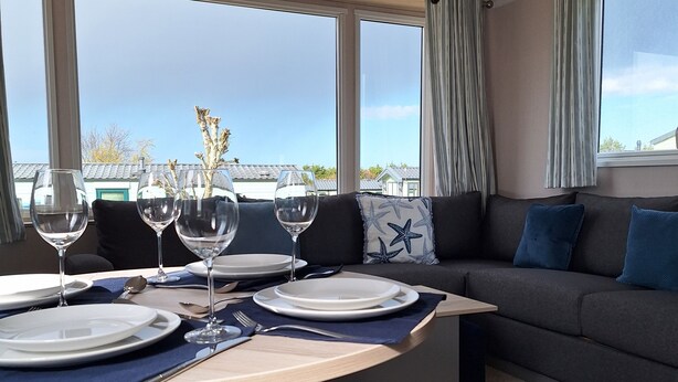 Un coin repas avec une table dressée pour quatre personnes, un canapé et une vue dégagée grâce à de grandes fenêtres.