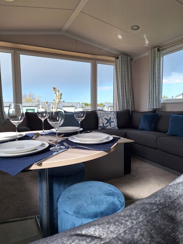 A dining area with a table set for four, a sofa, and a view through large windows. - Taigh na Mara, Holiday Home, St Andrews by the Sea (St Andrews)