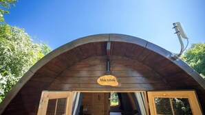 A wooden cabin with a curved roof, a sign reading 'MacAllan,' and a window on the right side.