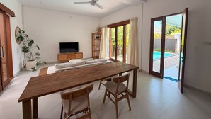 Amplia sala de estar con mesa de comedor de madera, sofá blanco y televisor.