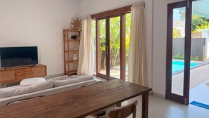 Un salón moderno con una mesa de comedor de madera, sofá blanco y televisor sobre un mueble de madera.