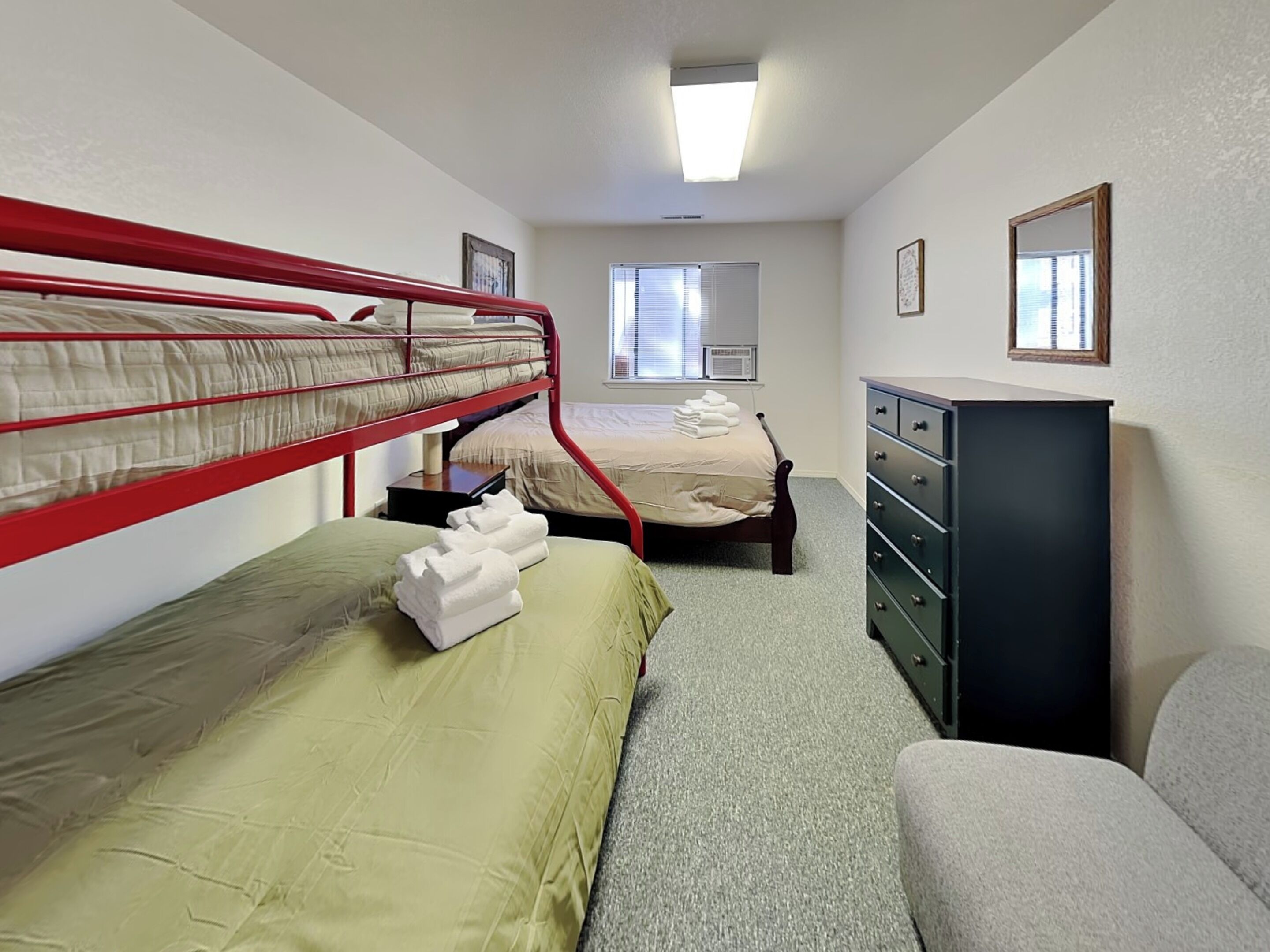 A room with bunk beds, a desk, a dresser, and a window.