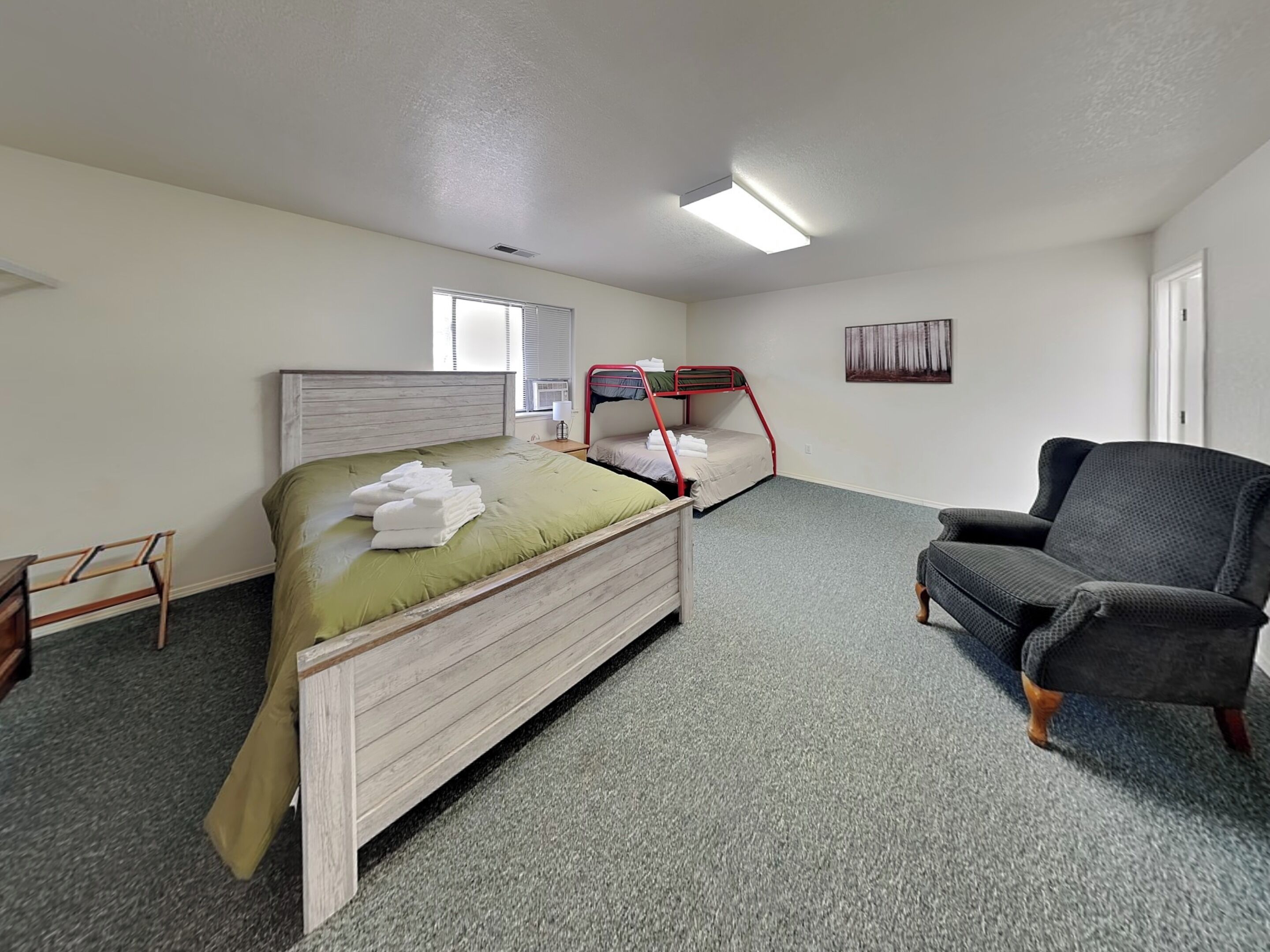 A room with a bunk bed, a chair, a small table, and a window.