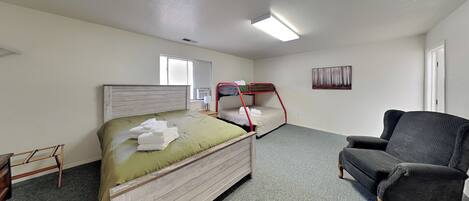 A room with a bunk bed, a chair, a small table, and a window.