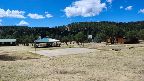 An open field with a pavilion, a basketball court, and a forested hill in the background. - Mountain View Cedar Lodge Cabin (Alto)