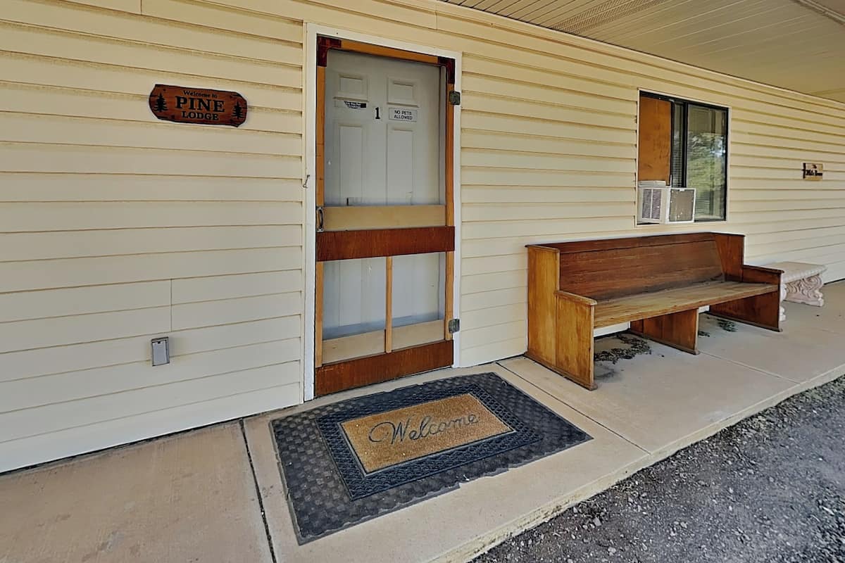 A Pine Lodge with a wooden bench outside, a welcome mat, and a door with a 'No Pets Allowed' sign.