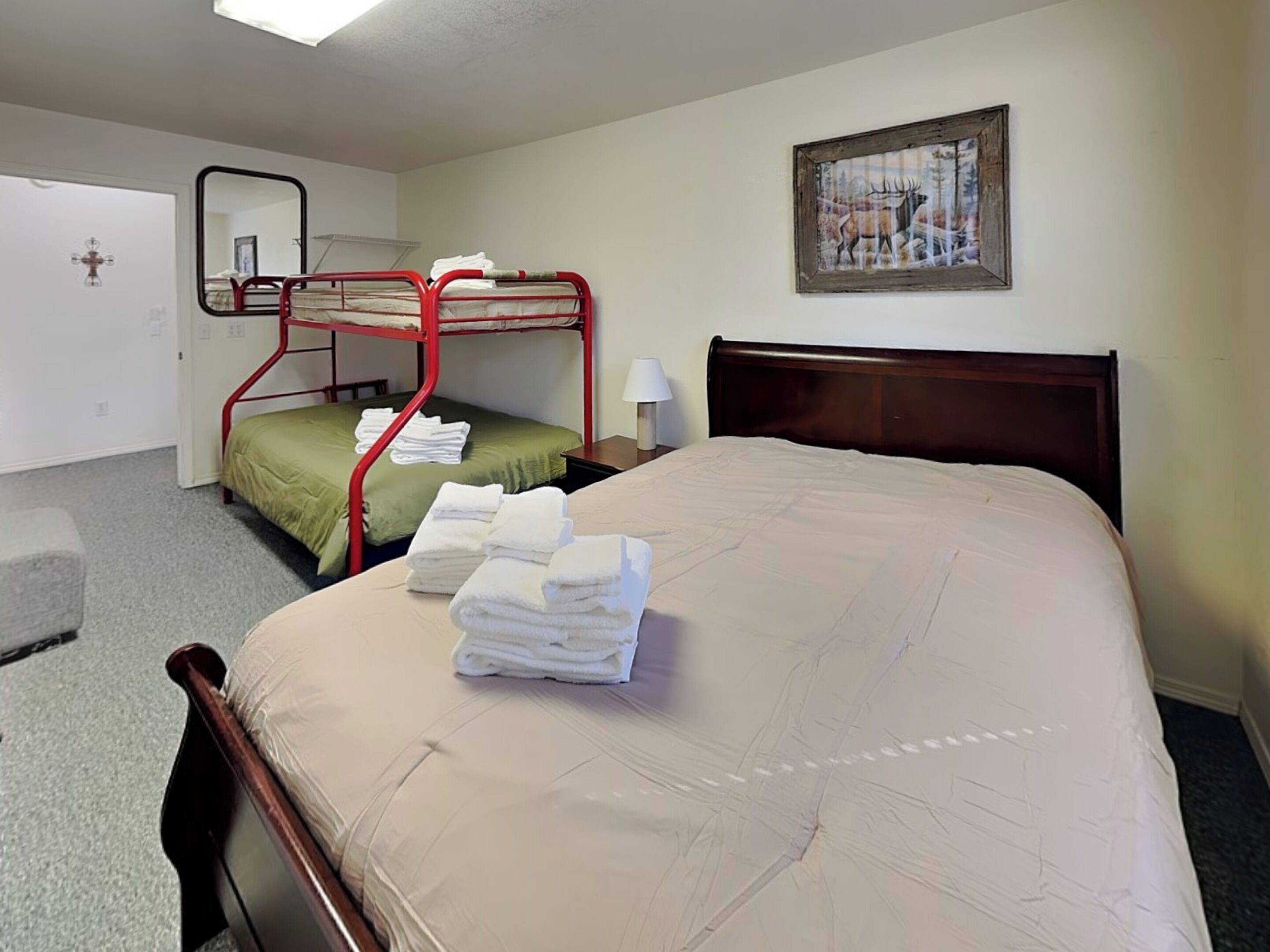 Habitación de hotel con literas, una cama individual, una mesita de noche con lámpara, un cuadro enmarcado en la pared y piso alfombrado.