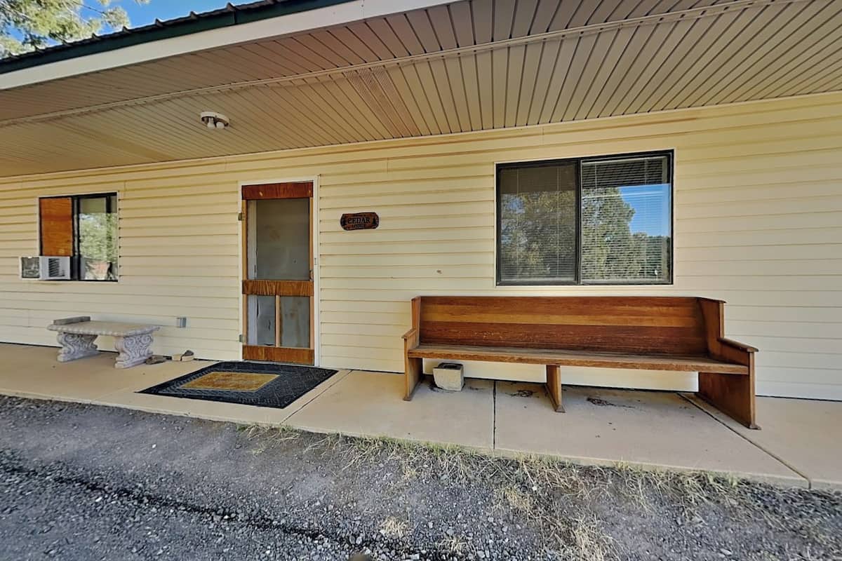 A single-story building with a wooden bench outside, a door, and a window with blinds.