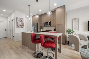 Una cocina moderna con una isla central, taburetes de bar, iluminación colgante y un microondas.