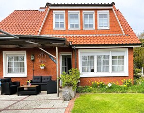 A two-story house with a red tiled roof, a brick facade, and a front porch with outdoor furniture. - ANKERHUUS NORDDEICH - Quiet apartment at the harbor with 2 bedrooms (Norddeich)