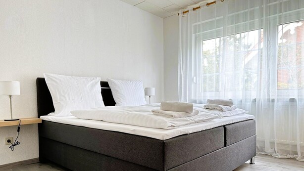 Un dormitorio moderno con una cama grande, lámparas de noche y cortinas translúcidas.