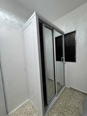 A room with a sliding glass door closet, a small window, and a speckled floor. - Brisa del Rio Jimenoa (Jarabacoa)