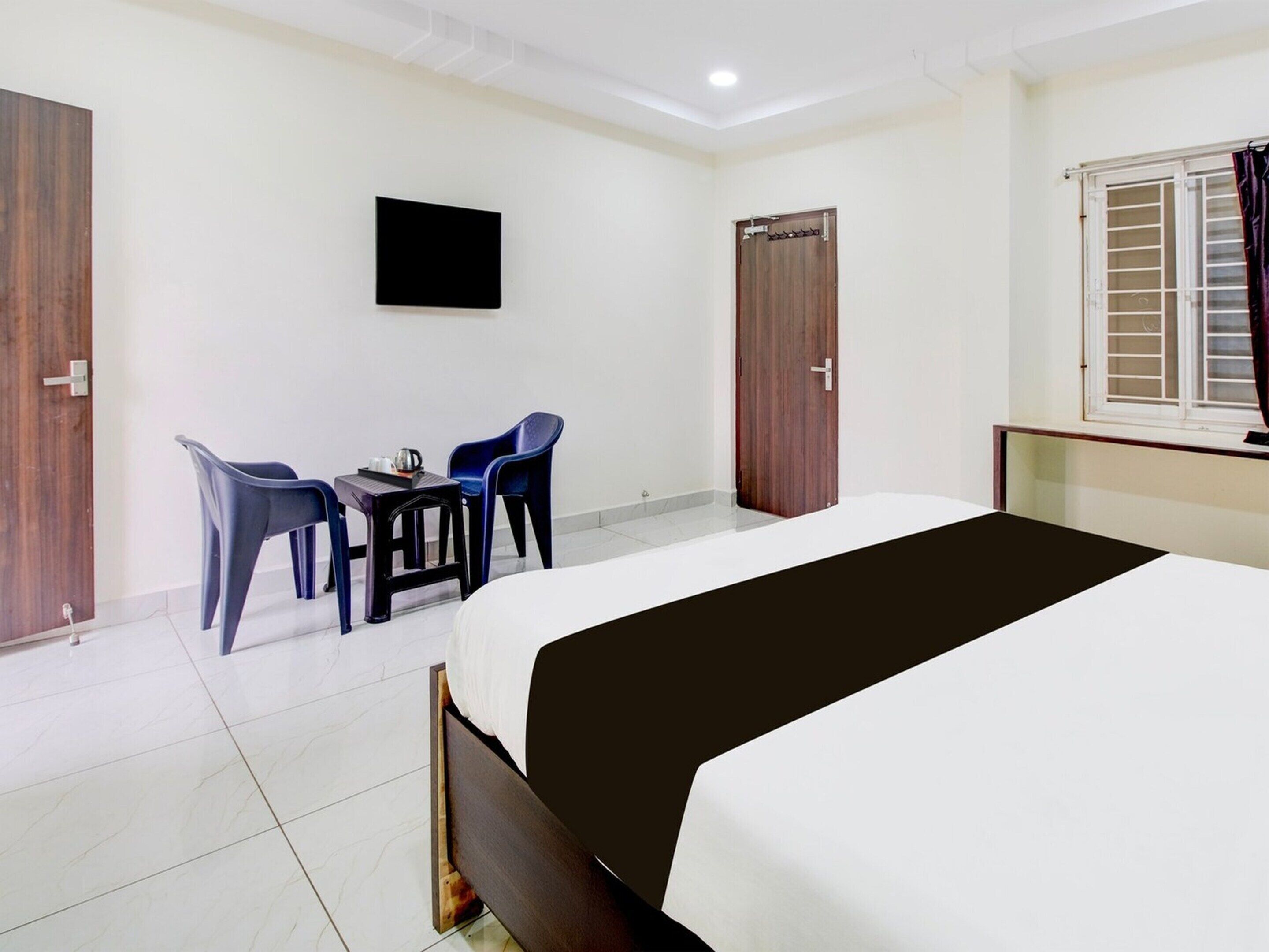 A hotel room with a bed, a TV mounted on the wall, a desk with chairs, and a window with curtains.