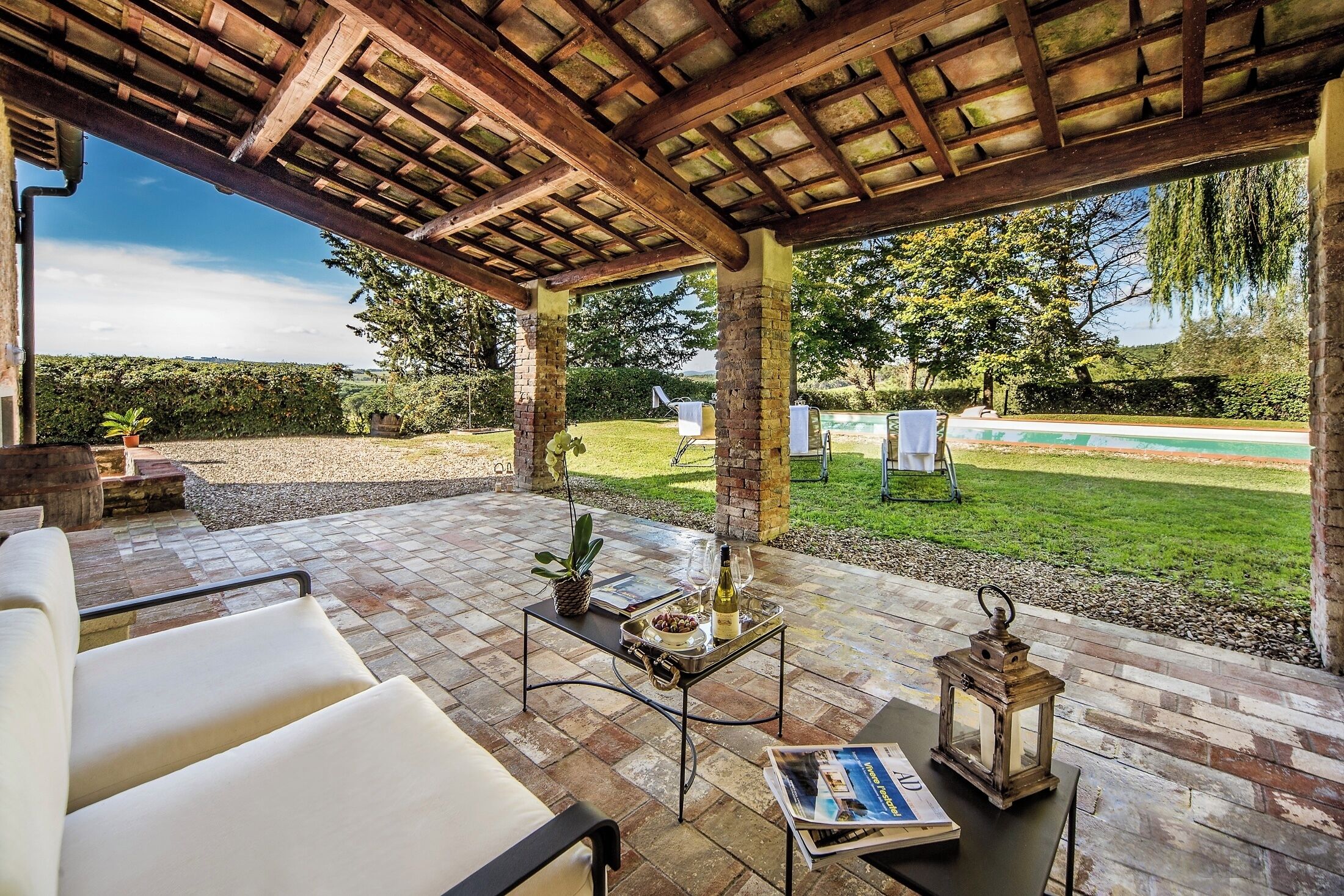 Eine Terrasse im Freien mit einer Pergola, Sitzgelegenheiten, einem Tisch mit Tablett und einer Laterne.