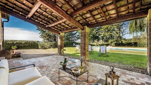 Een terras buiten met een pergola, zitplaatsen, een tafel met dienblad en een lantaarn.