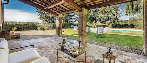 Eine Terrasse im Freien mit einer Pergola, Sitzgelegenheiten, einem Tisch mit Tablett und einer Laterne.