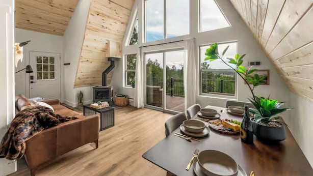 A spacious loft with a high ceiling, a fireplace, a dining area with a table set for four, and large windows offering a view of the outdoors. - The Timber Triangle-Views, Hot tub, Firepit (Florissant)
