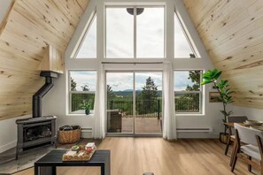 A high-ceilinged room with a wood stove, a dining area, and a balcony with a view of trees and mountains. - The Timber Triangle-Views, Hot tub, Firepit (Florissant)