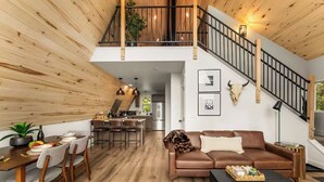 A spacious living area with a wooden ceiling, a dining table with chairs, a sofa, and a staircase with a railing. - The Timber Triangle-Views, Hot tub, Firepit (Florissant)