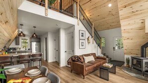 A spacious living area with a high ceiling, a staircase, a fireplace, and a dining area with a wooden table and chairs. - The Timber Triangle-Views, Hot tub, Firepit (Florissant)